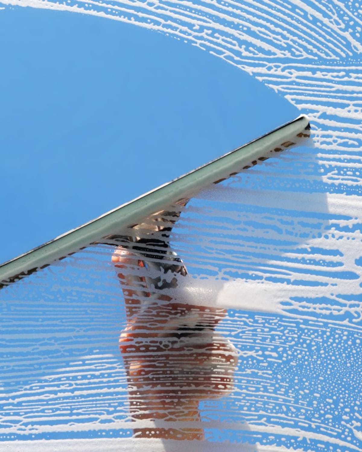 Squeegee blade pulling a clean stripe through soapy exterior glass under a blue sky, the finish Castle Rock, CO window walls deserve
